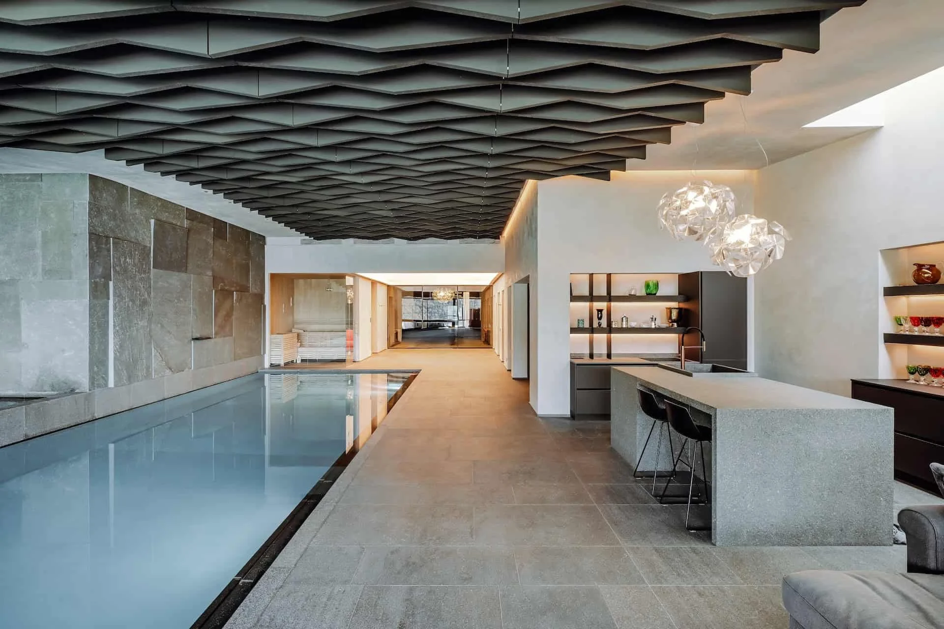 Moderne Indoor-Pool mit Holz- und Steinelementen, elegante Beleuchtung und offene Küchenbereich