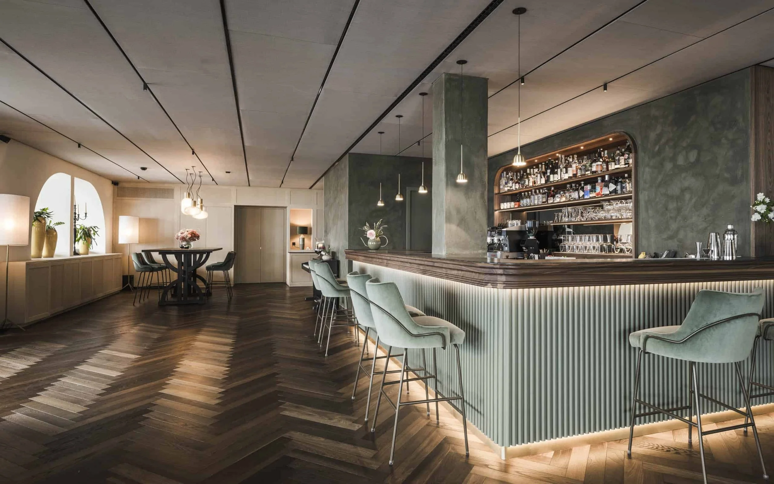 Ein elegantes Bar- und Restaurantbereich mit Lounge-Sitzen, Barhockern, einer Bar mit Flaschen und Gläsern, gemütlicher Beleuchtung und dekorativen Pflanzen.