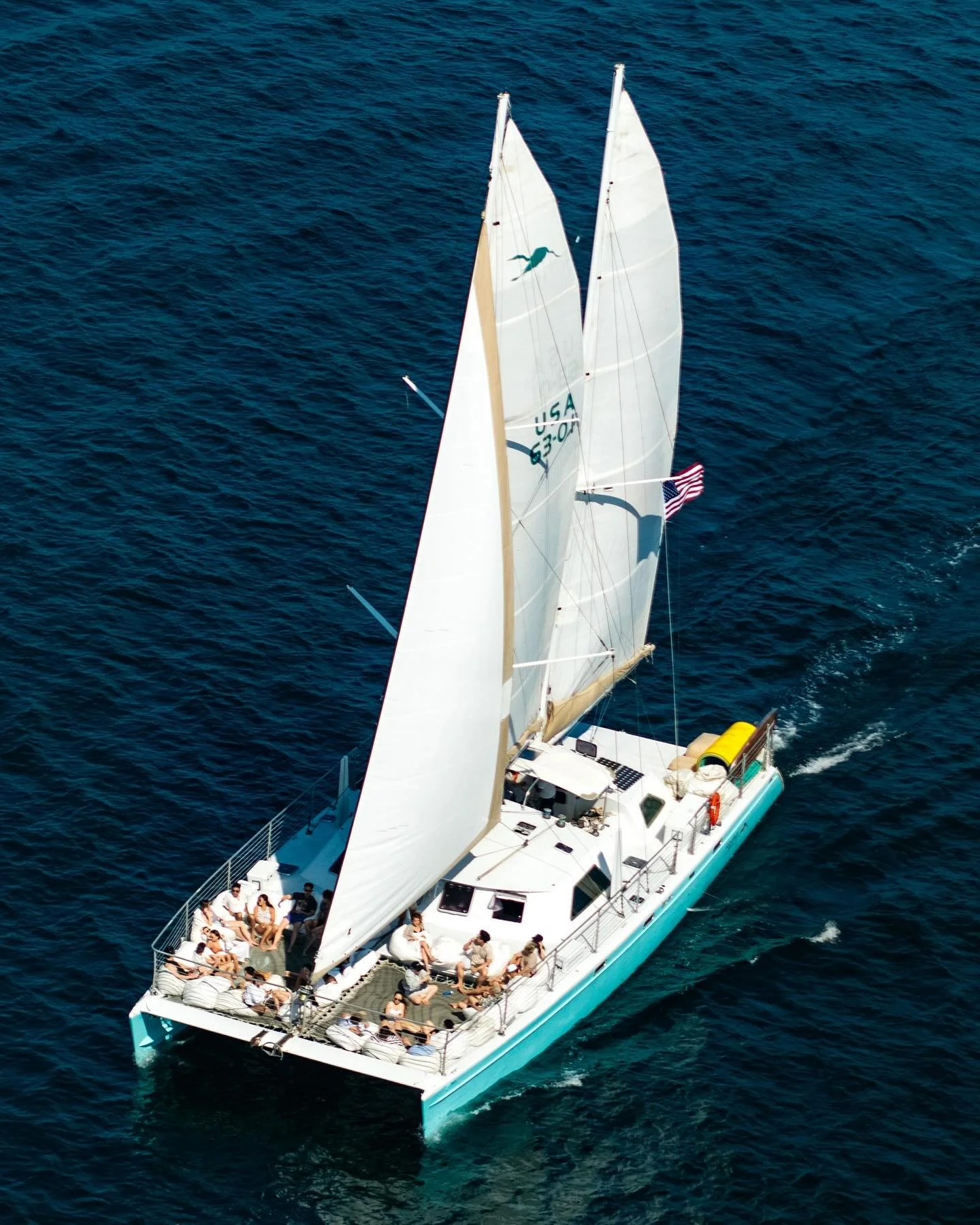 A group of people on a large sailing catamaran enjoying a day on the ocean with deep blue water.