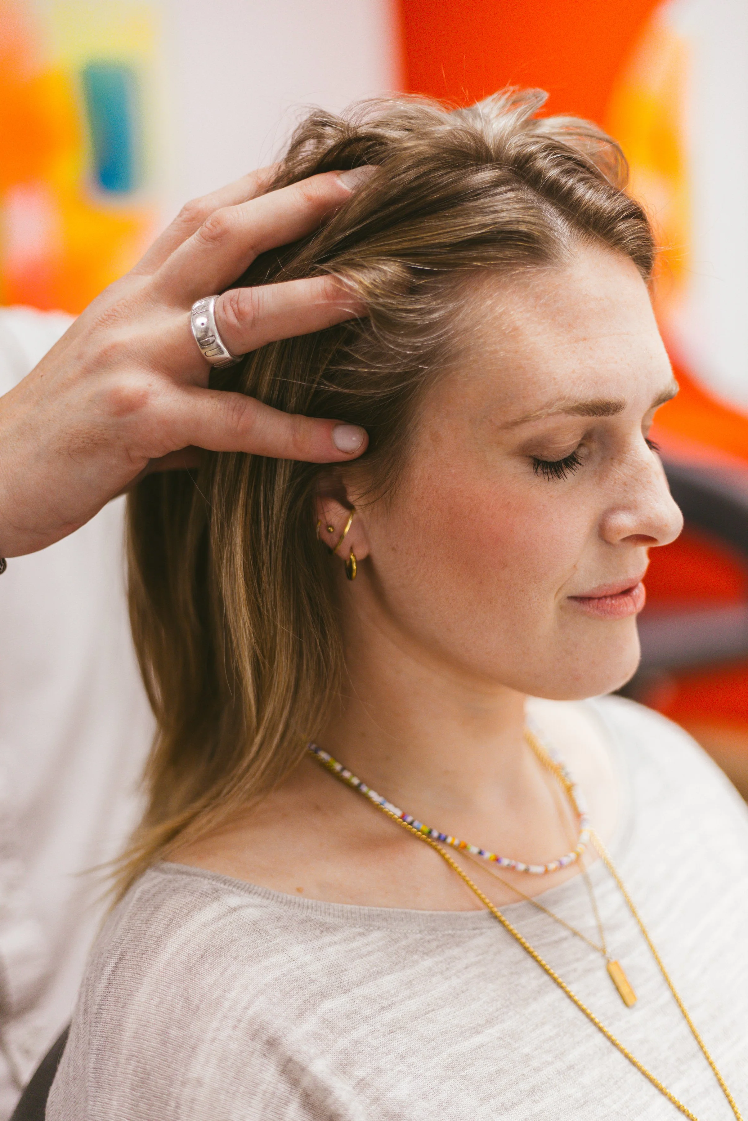 Eine Frau mit braunen Haaren, die eine professionelle Kopf- und Nackenmassage erhält, sitzend mit geschlossenen Augen.