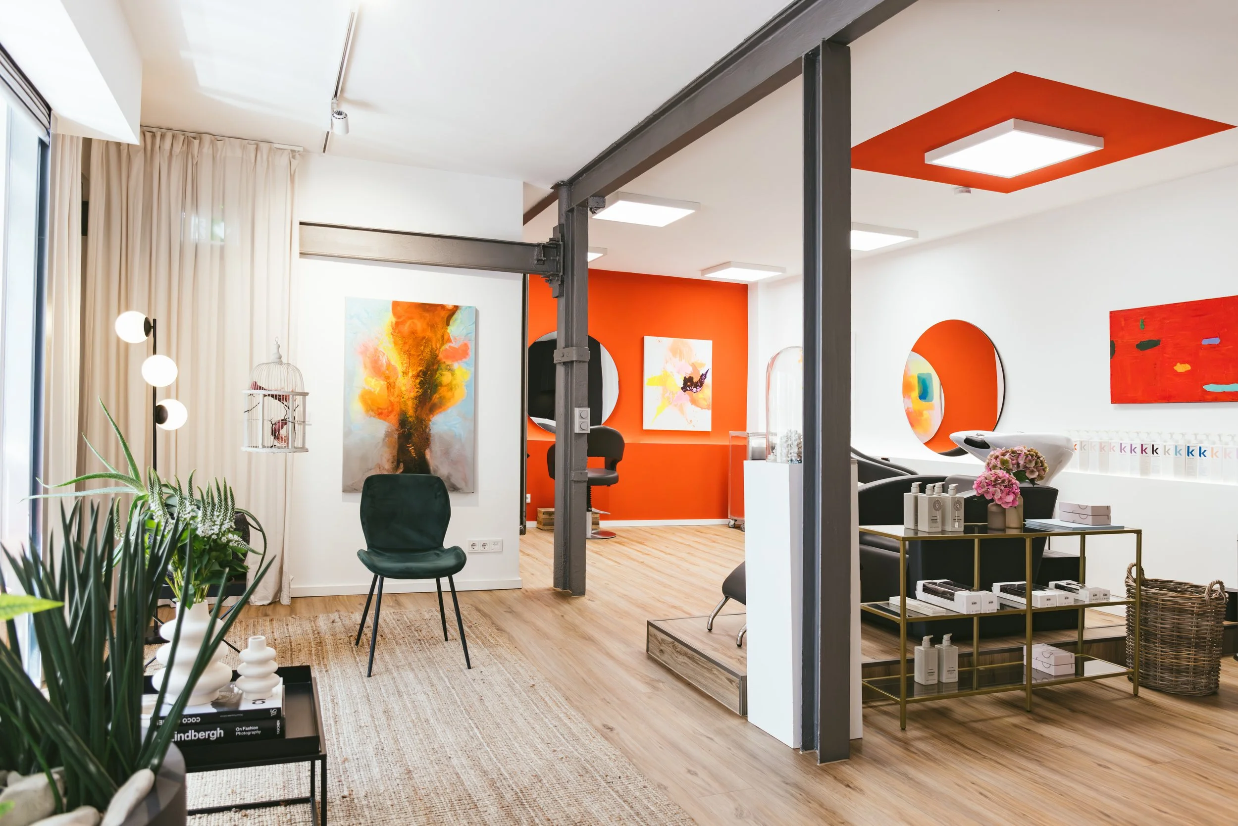 Innenraum eines modernen Friseursalons mit weißen Wänden, bunten Kunstwerken, Pflanzen, Stauraum und stilvoller Einrichtung.
