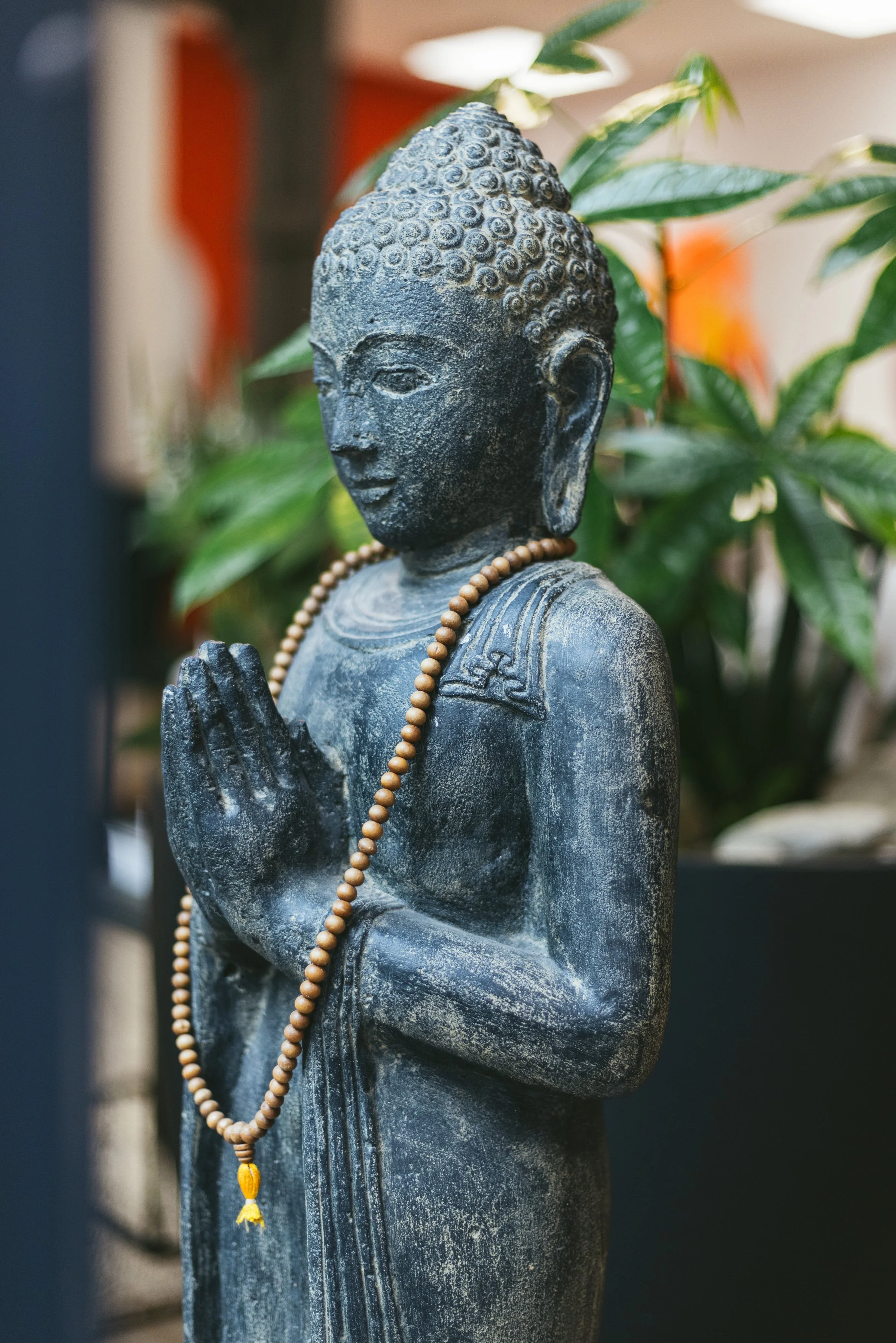 Steinschattierende Buddha-Statue mit Gebetsperlen, umgeben von grünen Pflanzen.