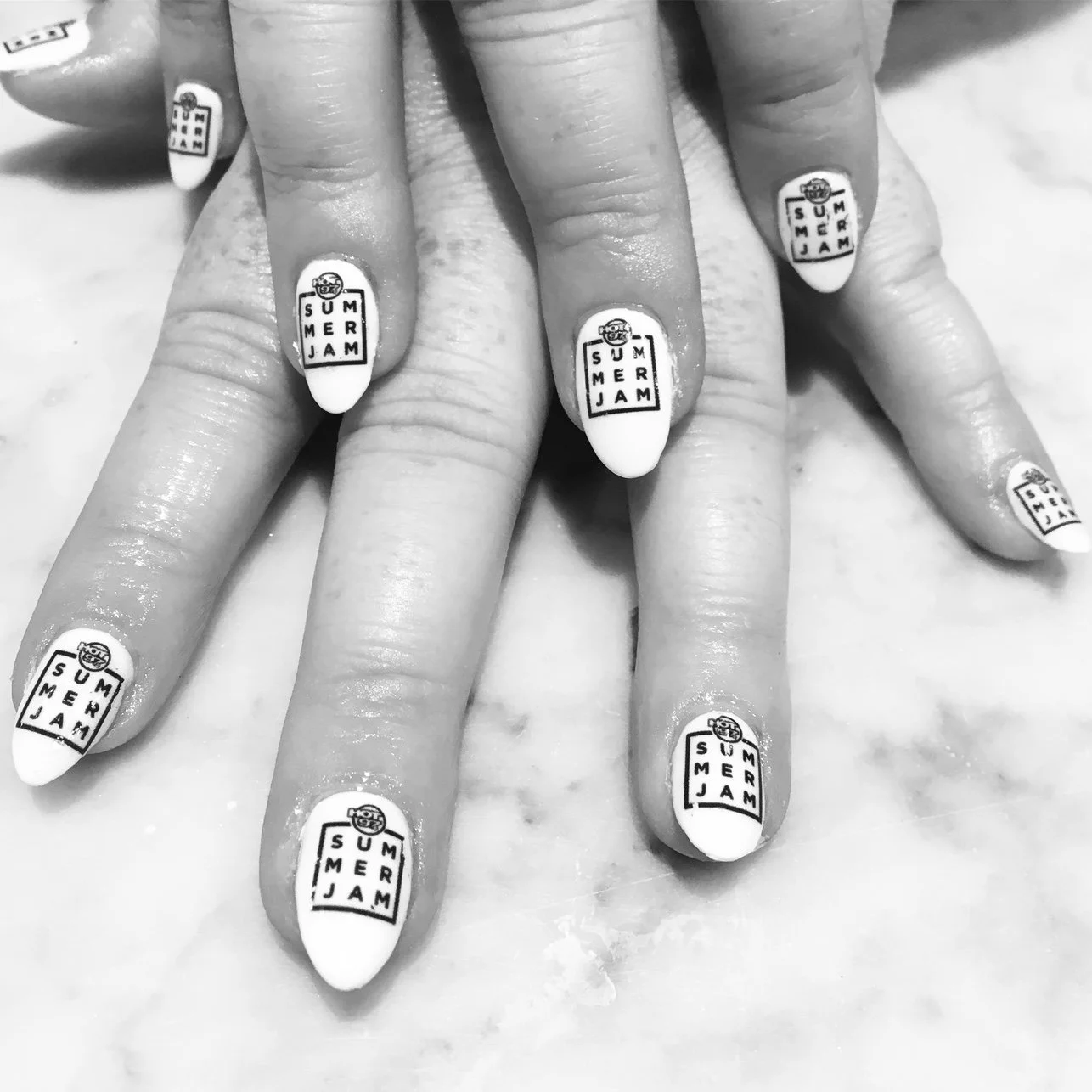 Close-up of fingers with nails painted white, displaying a 'Summer Jam' sticker design on each nail, in black and white.