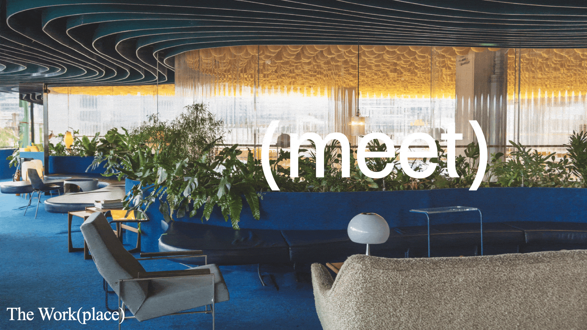 A modern indoor workspace with blue carpet, green plants, and a variety of chairs and tables. Large windows let in natural light, and the ceiling has a unique patterned design. The word '(meet)' is overlaid on the image, with 'The Work(place)' written in the bottom left corner.