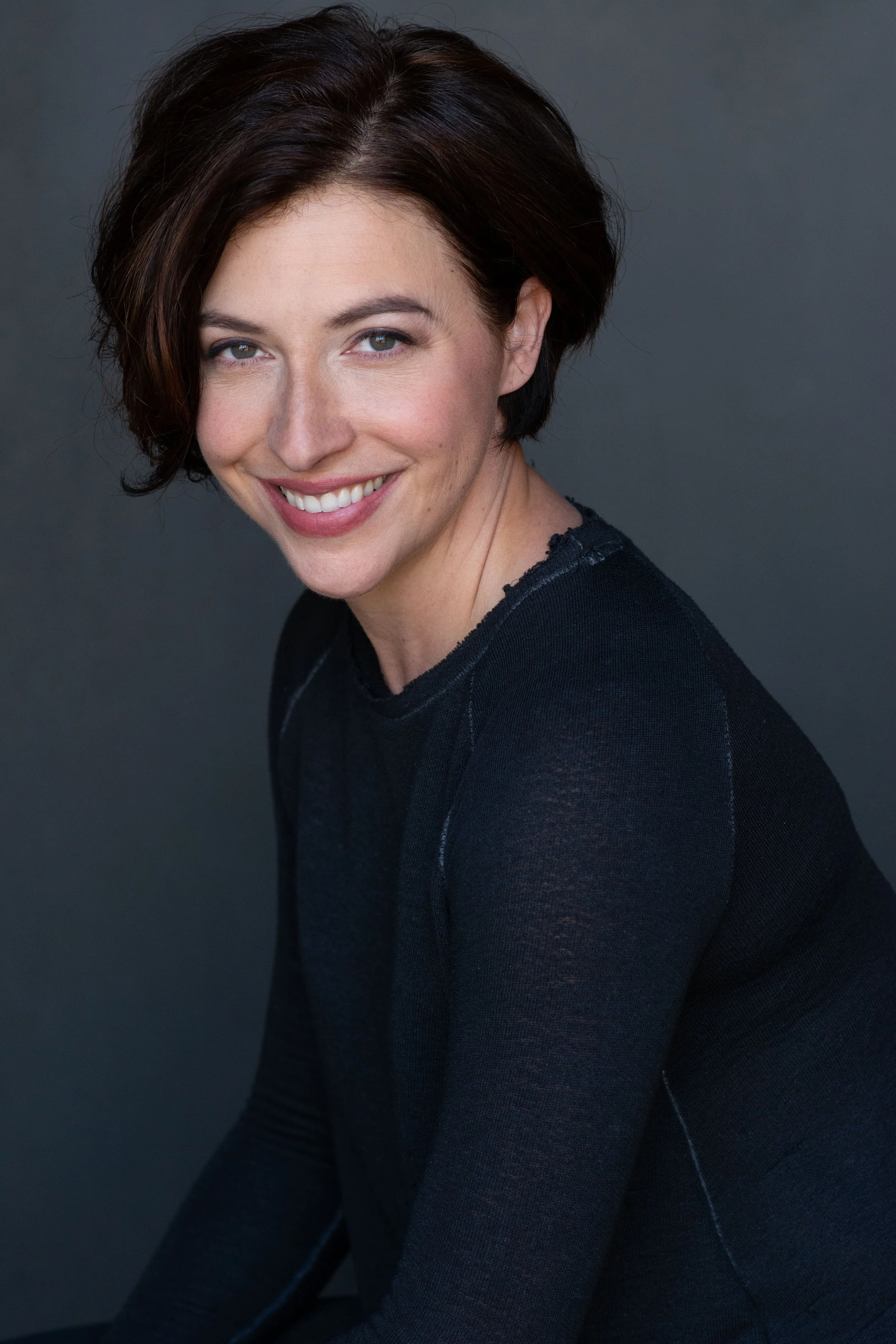 Natural smiling professional headshot of a woman with short dark hair and gentle smile against a gray background in Tacoma Washington