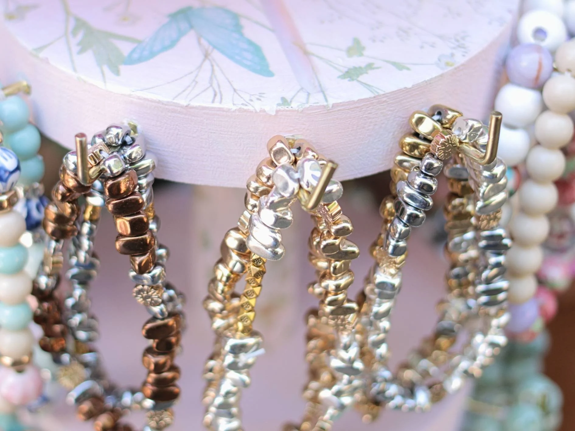 Close-up of assorted beaded bracelets hanging on display, with a decorative box with botanical illustrations in the background.