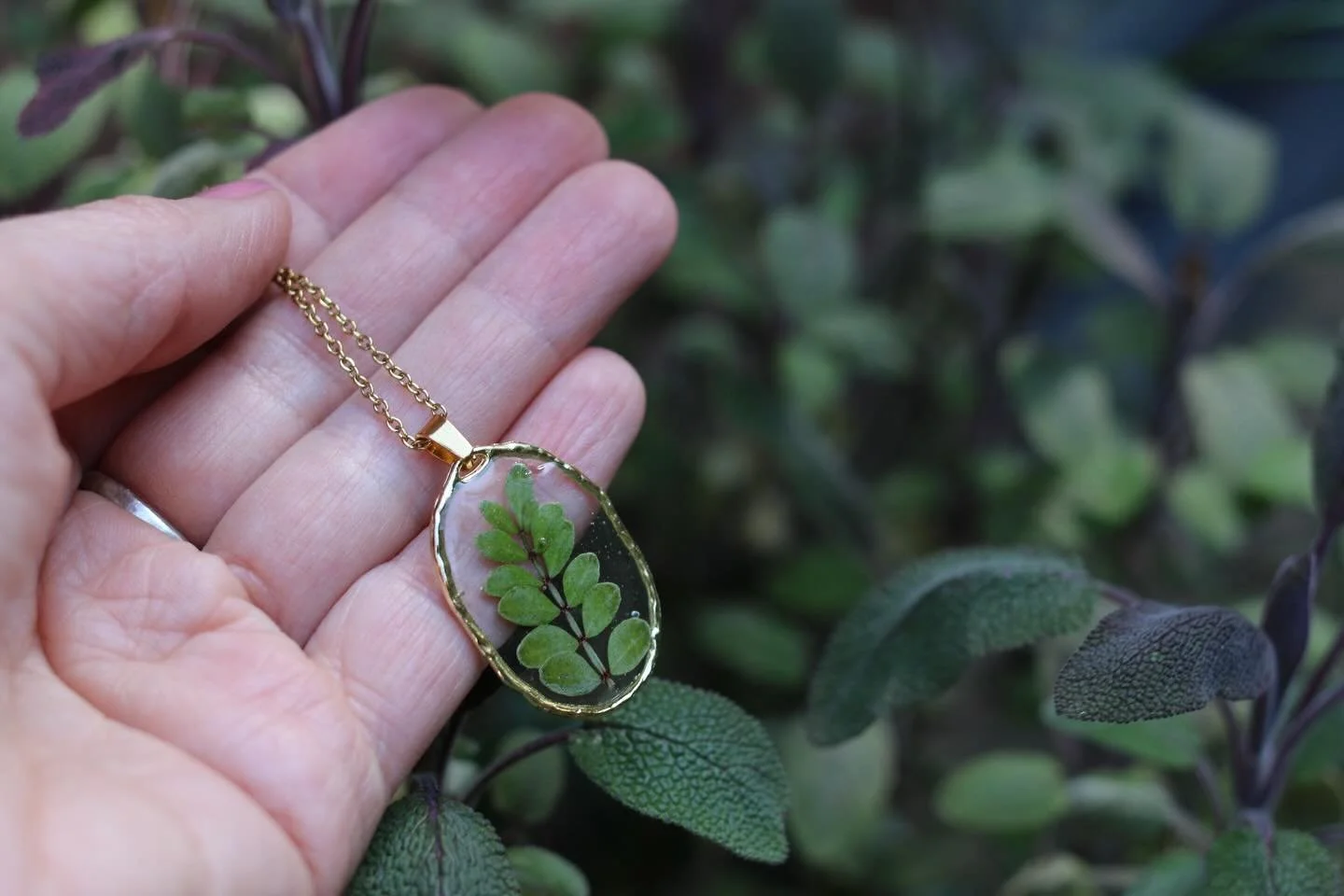 Pressed Leaf Oval Pendant Necklace

Earthy and calming, this handcrafted necklace features real pressed plant leaves, carefully preserved in clear resin to showcase their natural structure and soft green tones. Each detail of the leaf is captured, cr