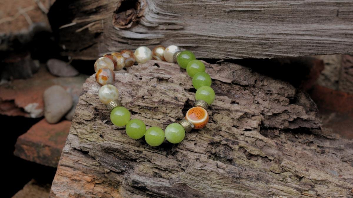 Beaded bracelet with green, white, and orange beads resting on a piece of rough, textured wood.