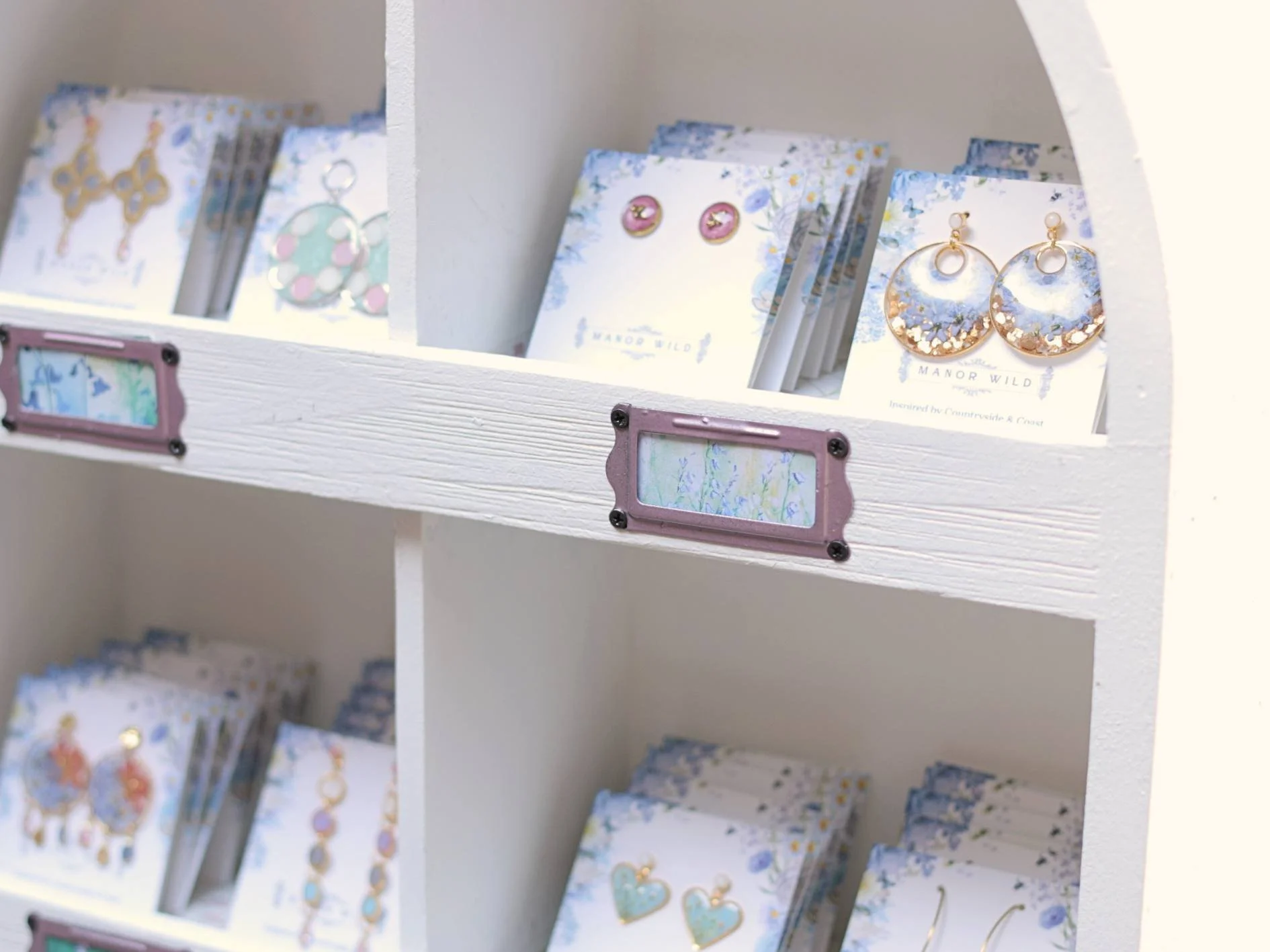 Display shelf with decorative gift tags and jewelry items such as earrings featuring floral and heart designs.