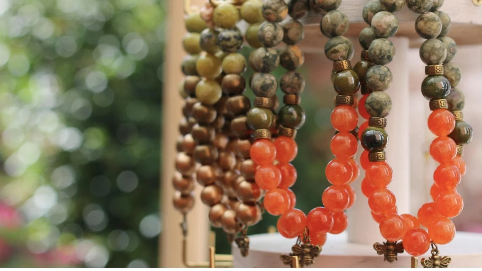 Close-up of colorful beaded necklaces hanging with a blurred outdoor background.
