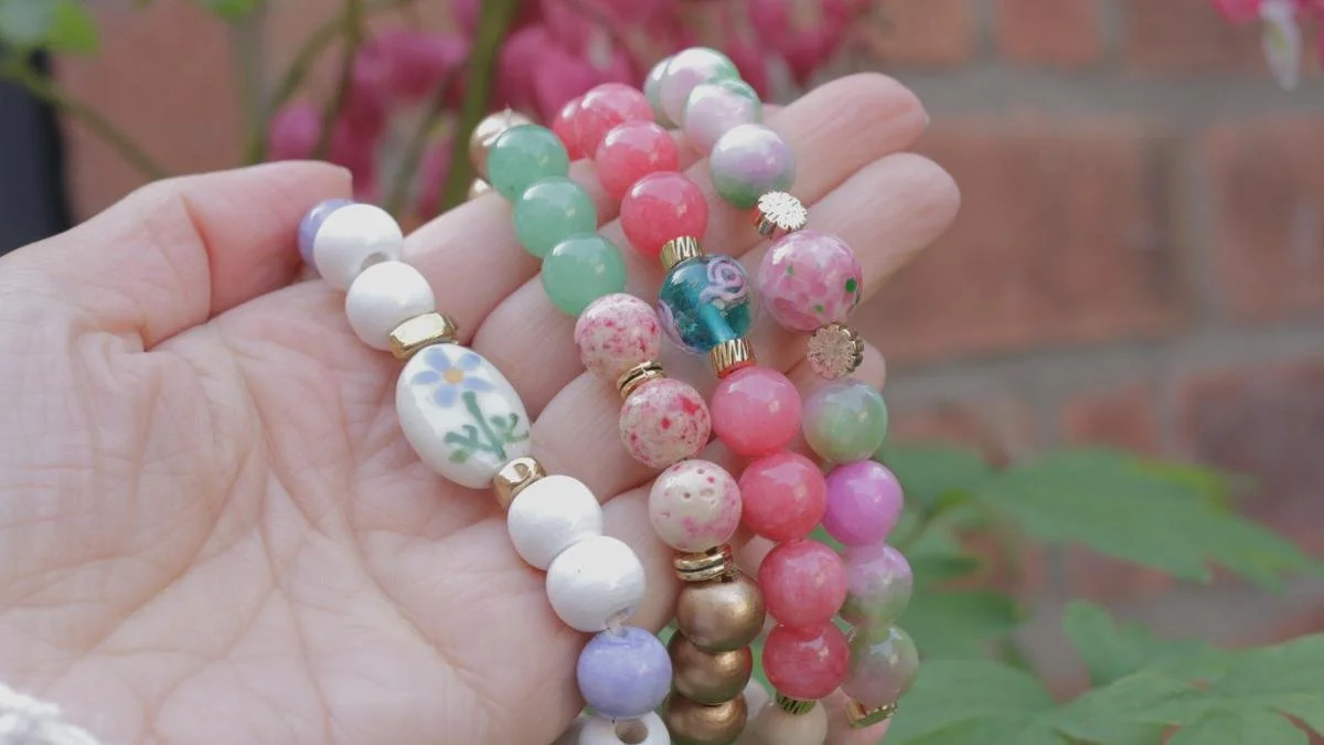 Hand holding colorful beaded bracelets with pink flowers and green leaves in the background