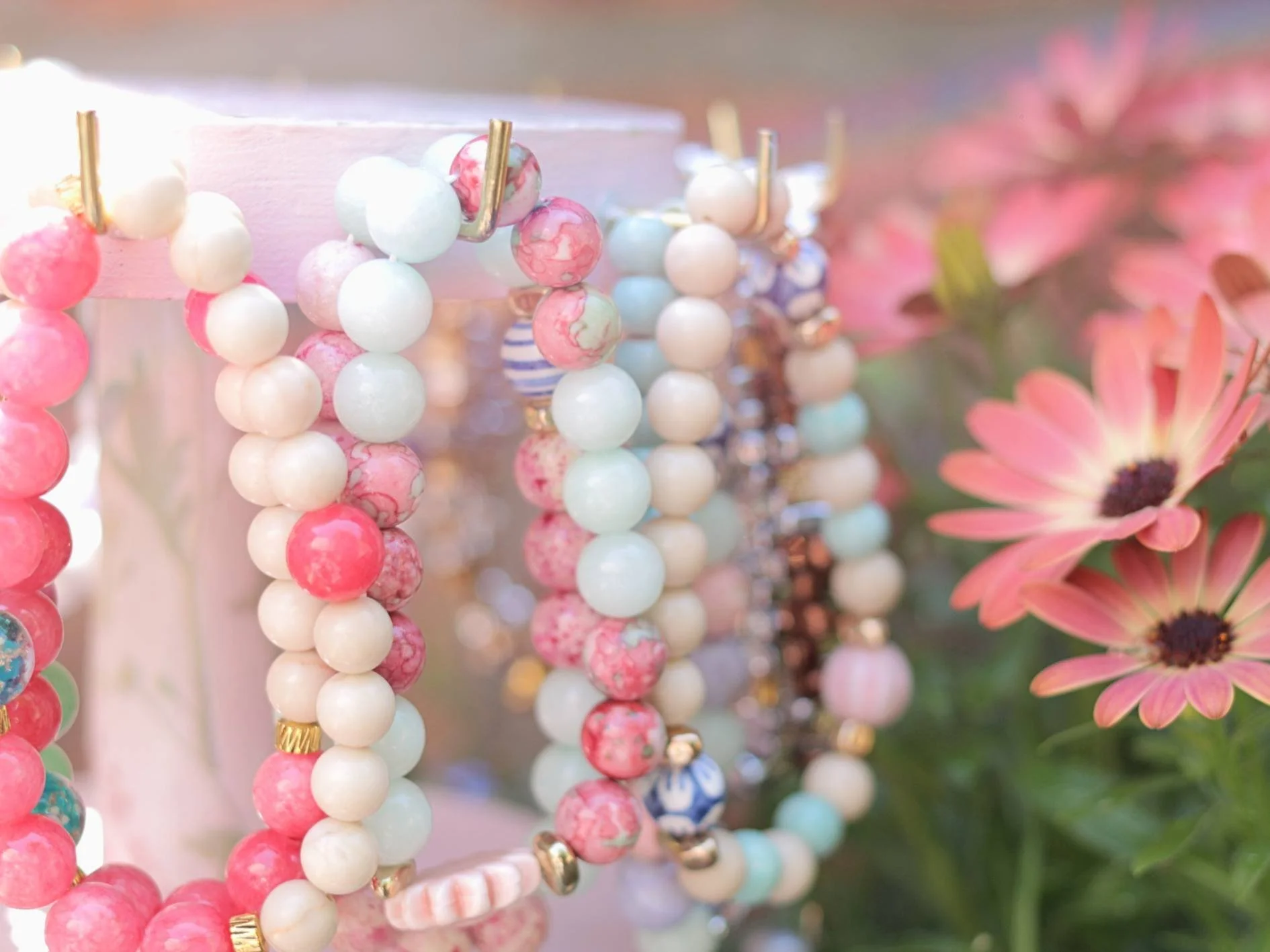 A close-up of colorful bead necklaces hanging with pink flowers in the background.