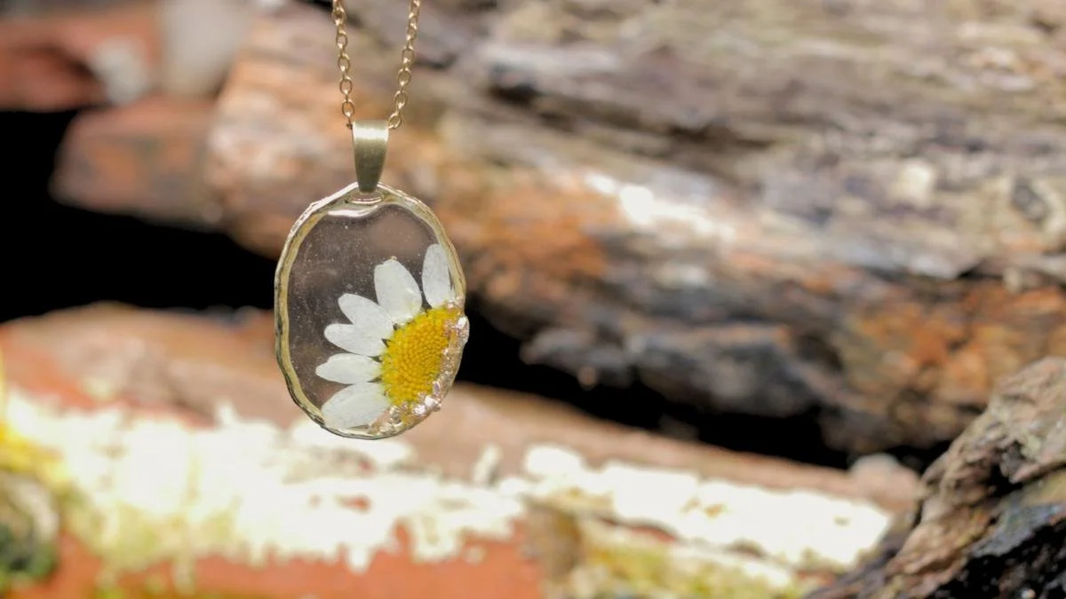A pendant with a daisy flower preserved inside a clear resin, hanging from a gold chain.