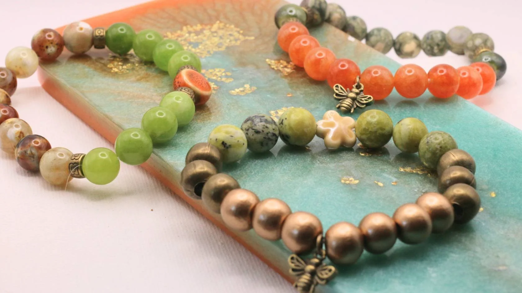 Colorful beaded bracelets with butterfly and flower charms on an art-covered surface.