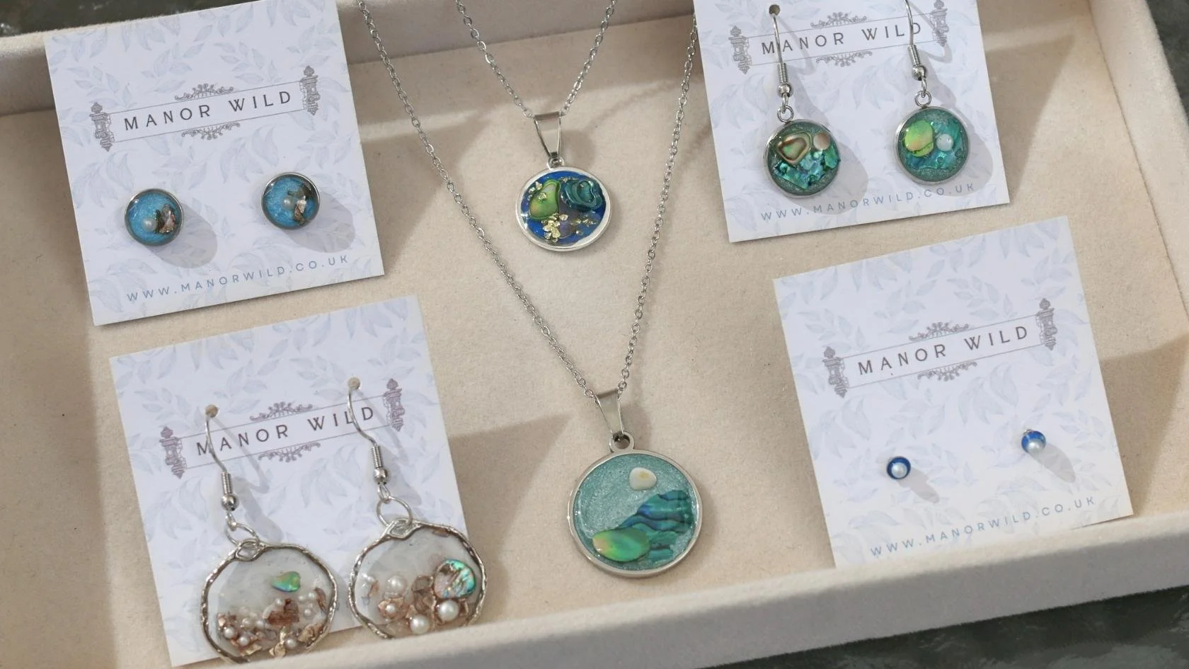 Jewelry display with earrings and necklaces featuring aquatic-themed designs and pearls, arranged on white cards labeled Manor Wild.