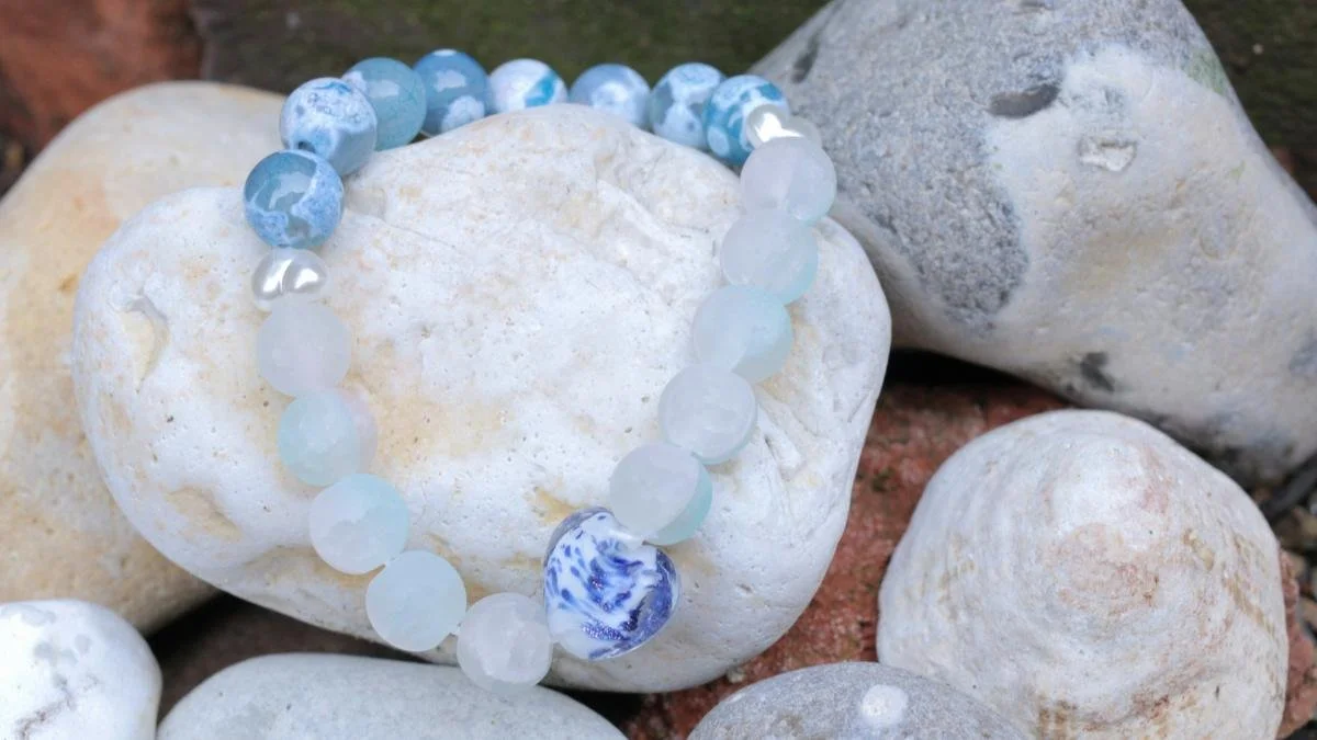 A beaded bracelet with blue, white, and marbled beads resting on white and gray rocks.