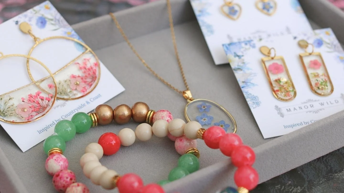 Fashion jewelry set with gold-colored earrings, a necklace, and beaded bracelets featuring pink, green, white, and gold beads, displayed on white cards with floral and jewelry-themed designs.