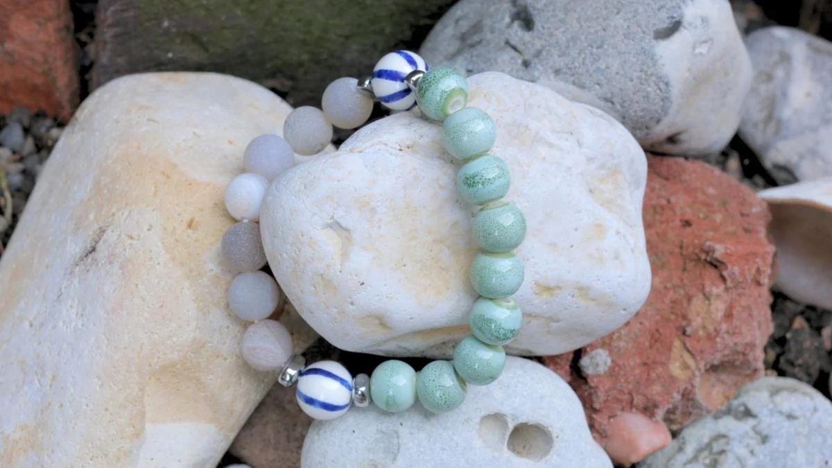 Beaded bracelet with white, blue, and green beads resting on rocks.