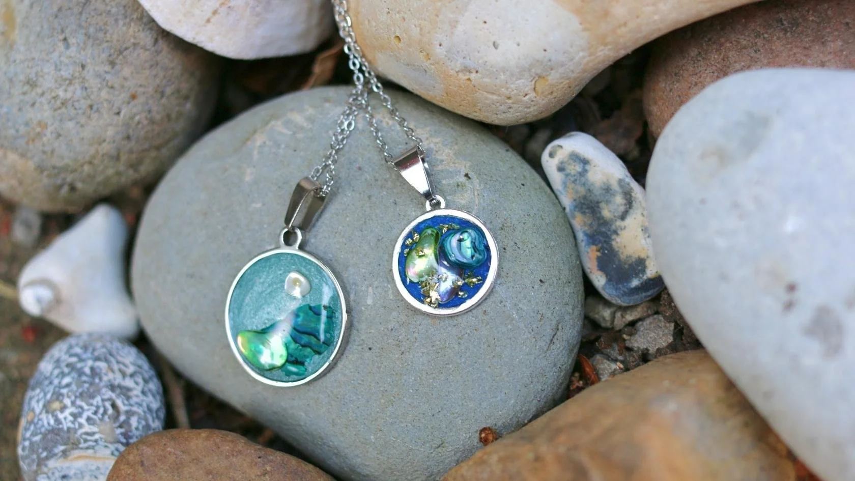 Two circular pendants with colorful, abstract designs lying on a bed of rocks.
