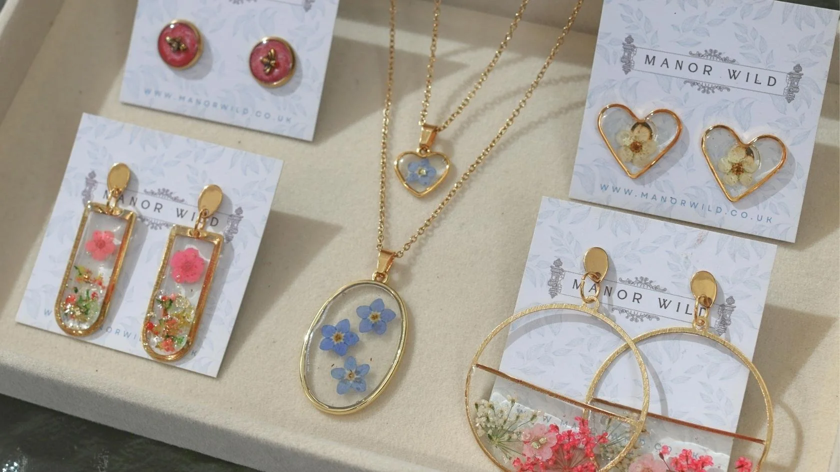 Jewelry display featuring gold earrings and necklaces with pressed flowers and floral designs on the pendants and earrings.