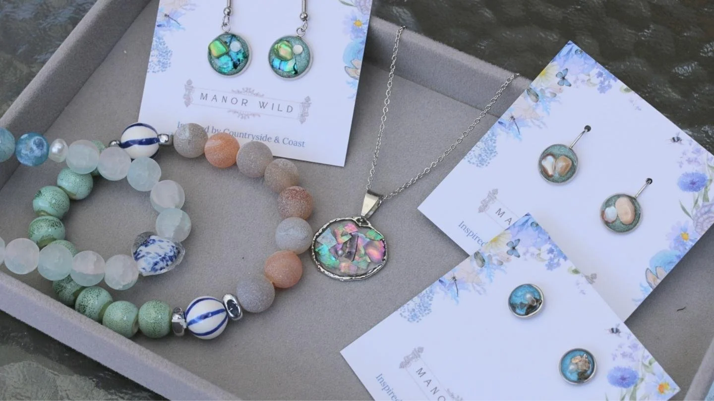 Assorted jewelry including earrings, necklaces, and bracelets displayed on cards with floral and butterfly patterns in a grey box, with water visible on one side.