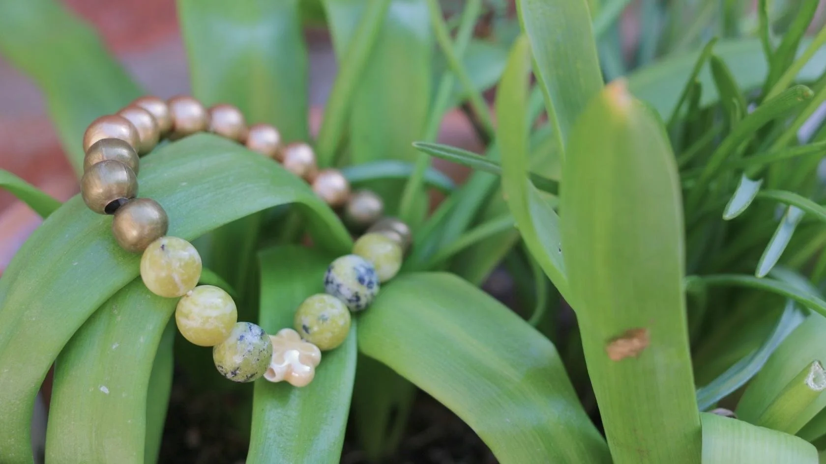 A beaded bracelet resting on green leaves and grass.