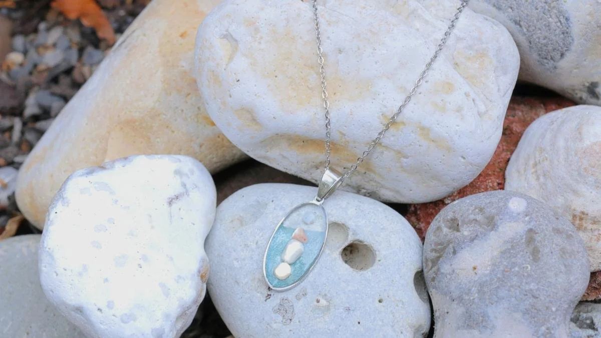 Silver necklace with a pendant containing small colorful stones, resting on white, gray, and reddish stones.