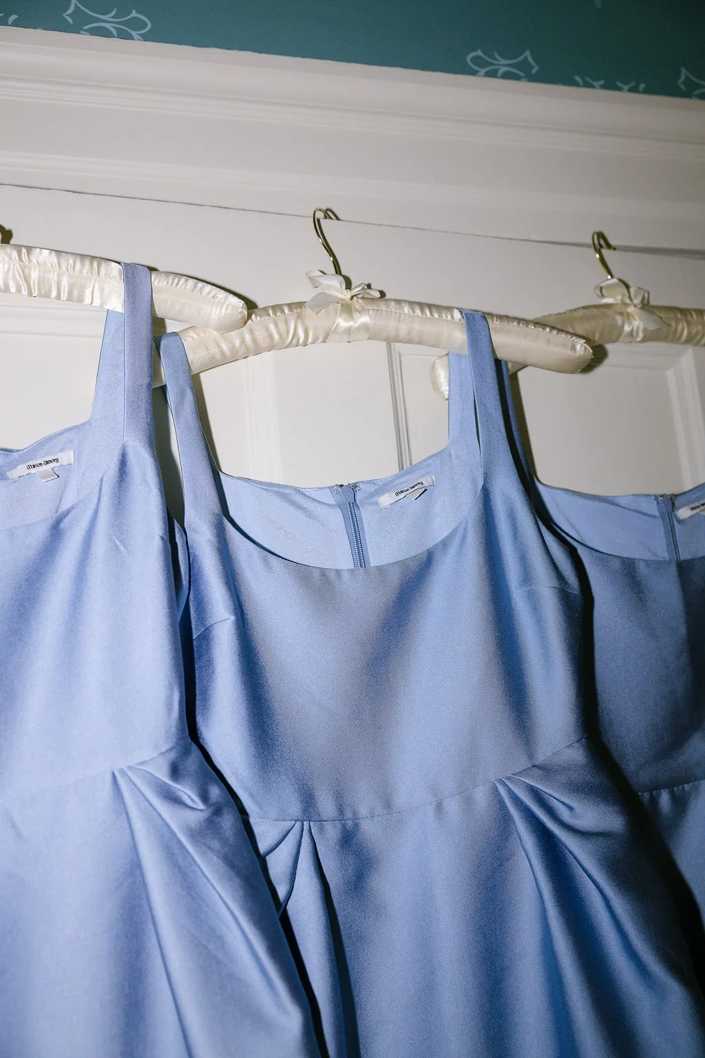 Three light blue dresses hanging on padded hangers with bows, suspended on a rod.