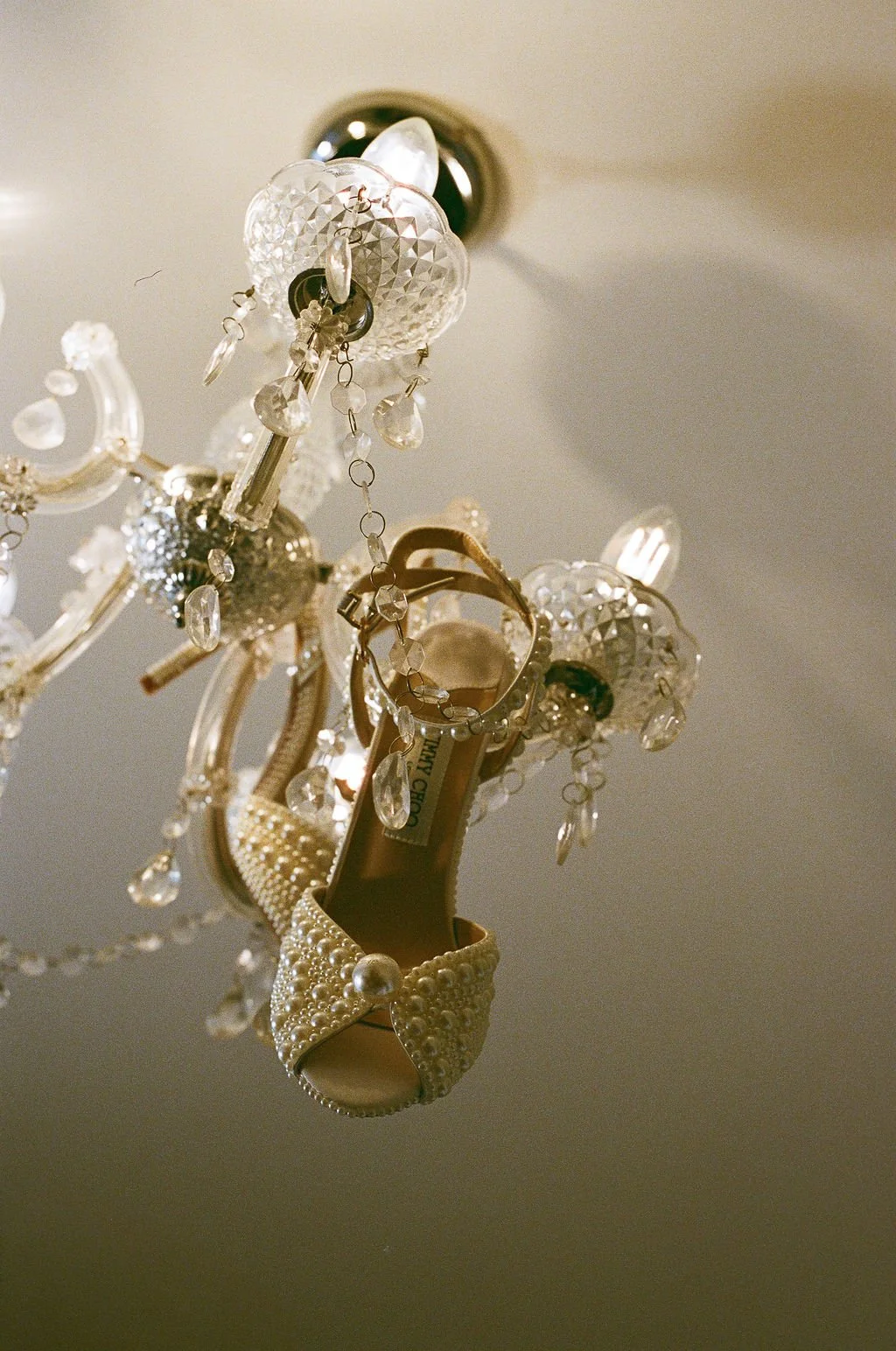 A chandelier is decorated with pearl-embellished high heel shoes, jewelry, and crystal ornaments.