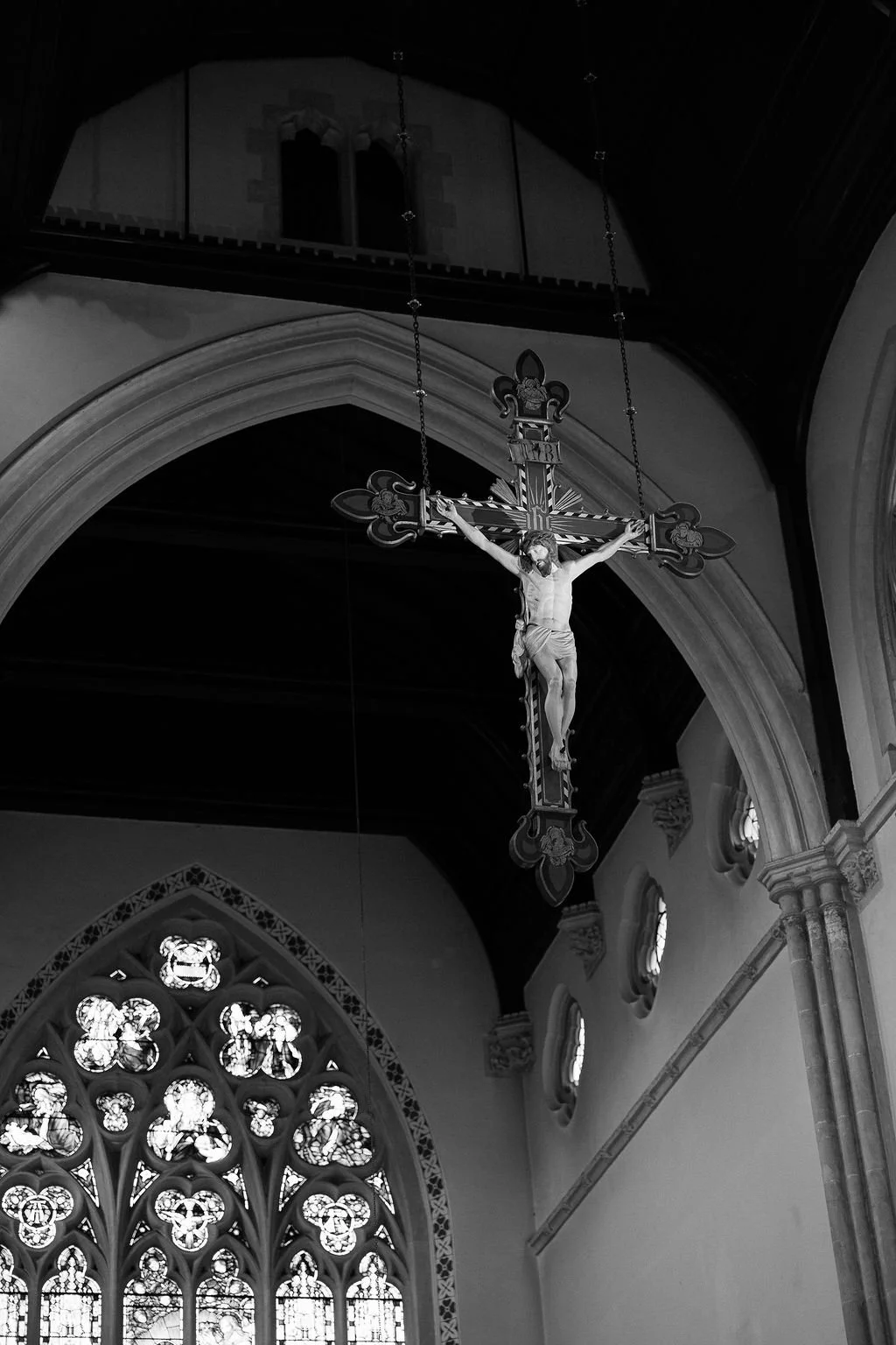 Black and white photo of a Christian church featuring a crucifix with Jesus hanging on the cross, located above stained glass windows.