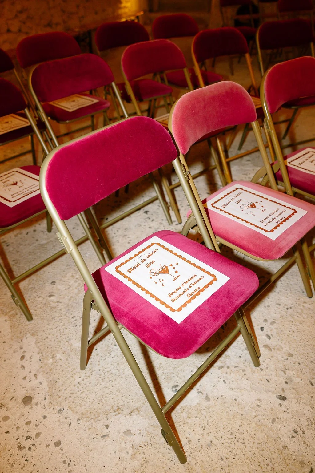 Multiple pink velvet chairs arranged in rows in an indoor setting, with papers placed on some seats.