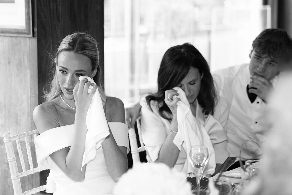 Three people sitting at a table, two women and one young man, crying and wiping tears during a meal in a restaurant.