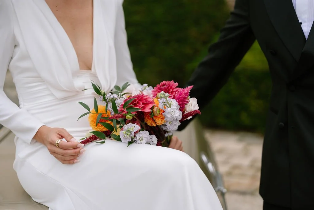Woman in white dress holding a colorful bouquet of flowers during a wedding ceremony, with man in a black suit beside her.