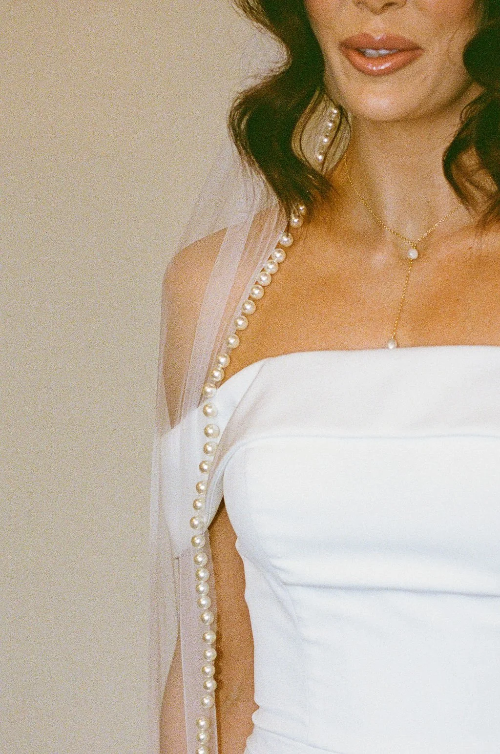 Close-up of a woman wearing a white dress with pearl embellishments, layered pearl jewelry, and makeup with glossy lips.