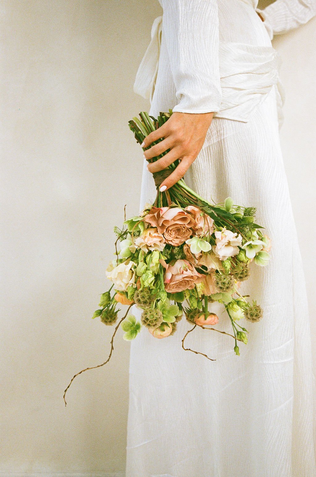 Person in white dress holding a bouquet of light pink and white flowers