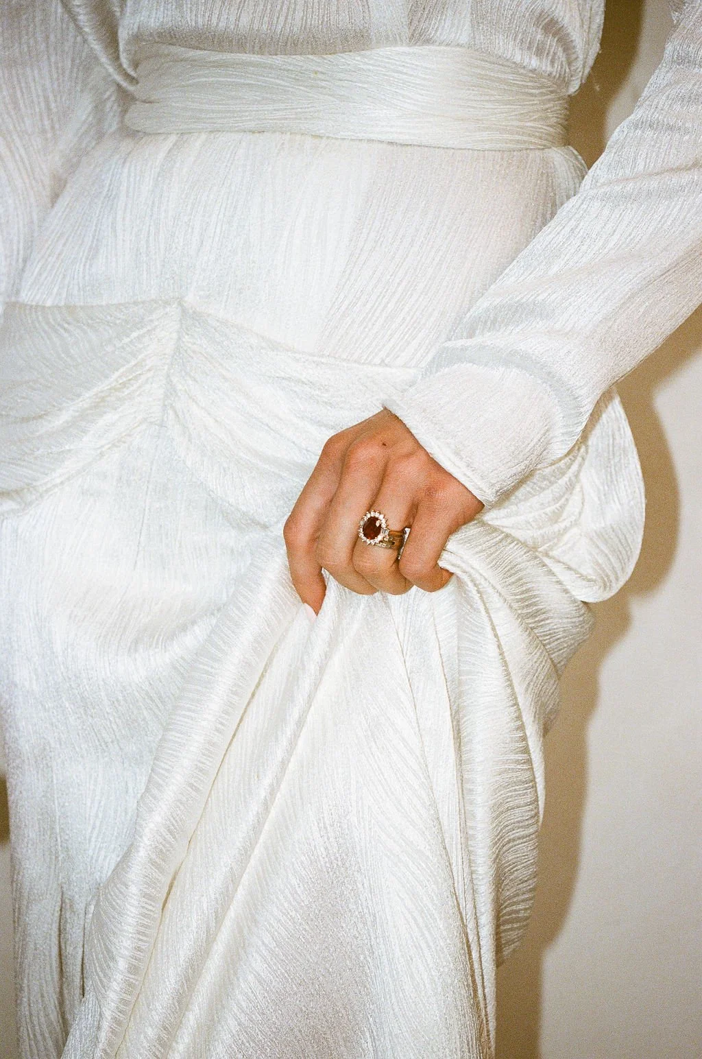 Close-up of a person in a white textured dress holding a white fabric with their hand, wearing rings on their finger.