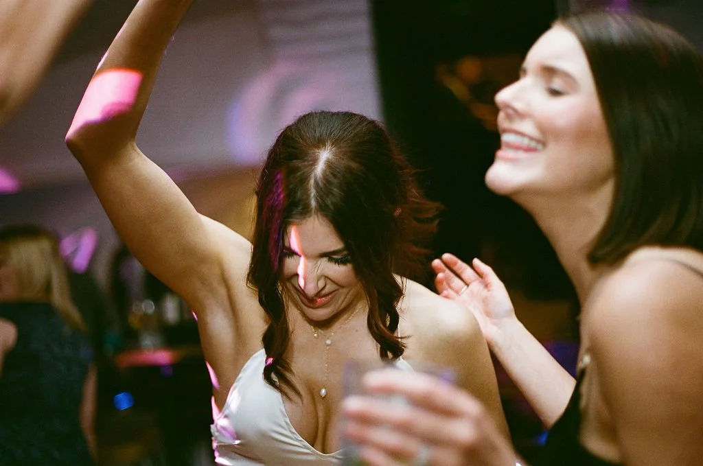 Two women dancing and smiling at a party or club, with one woman holding a drink and enjoying the moment.