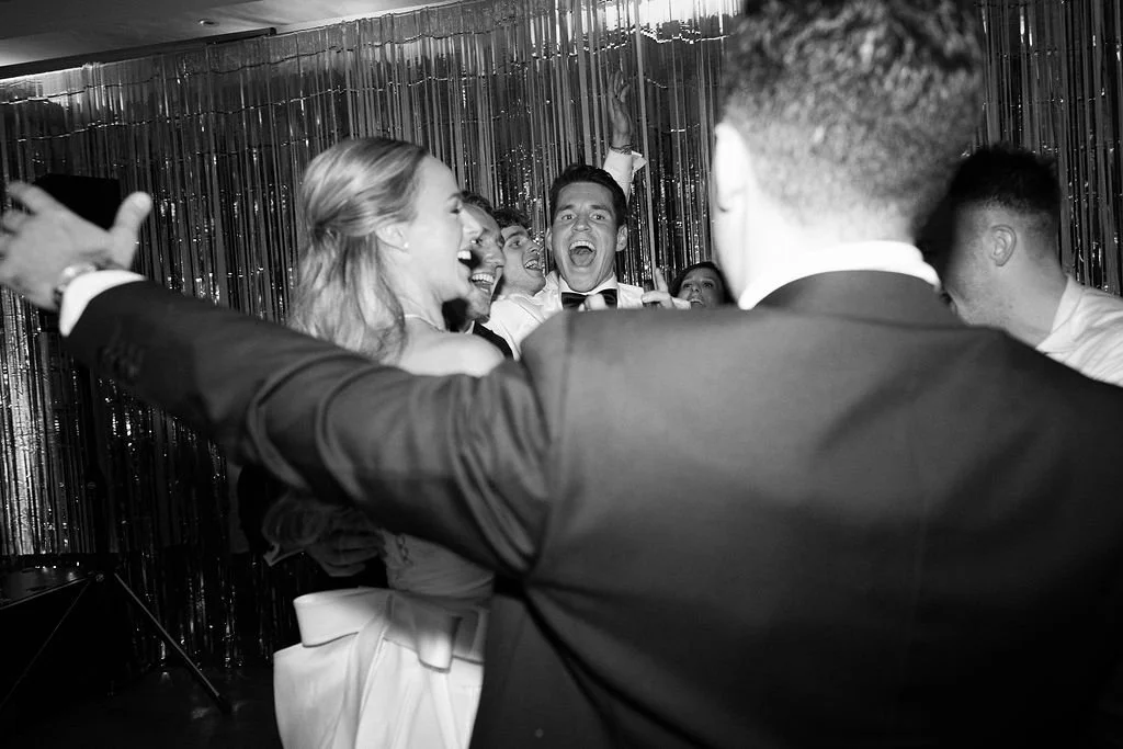 Group of people smiling and celebrating at a party with metallic curtain in the background.