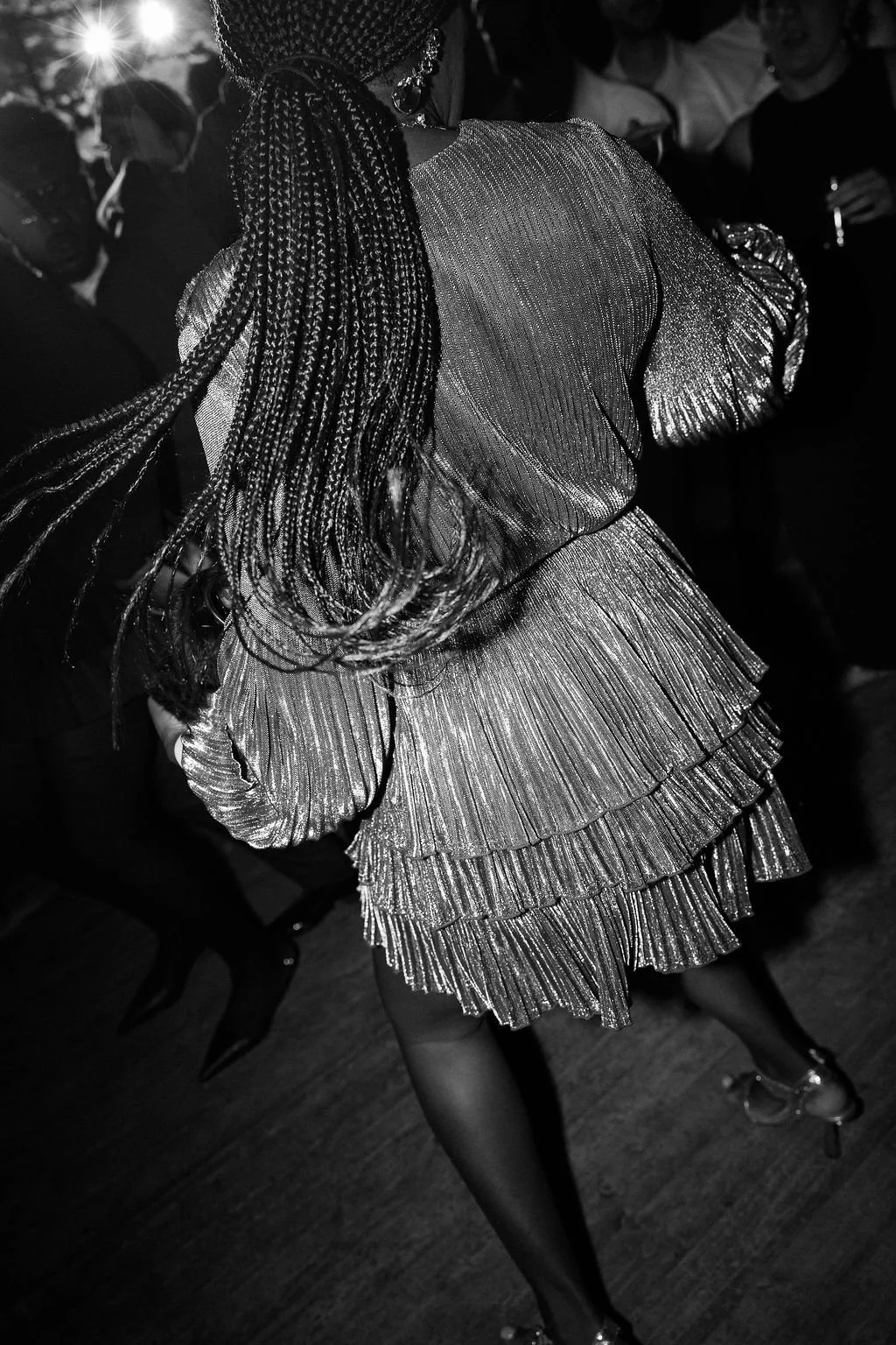 Woman with long, braided hair wearing a shiny, layered, pleated dress at a party or event.