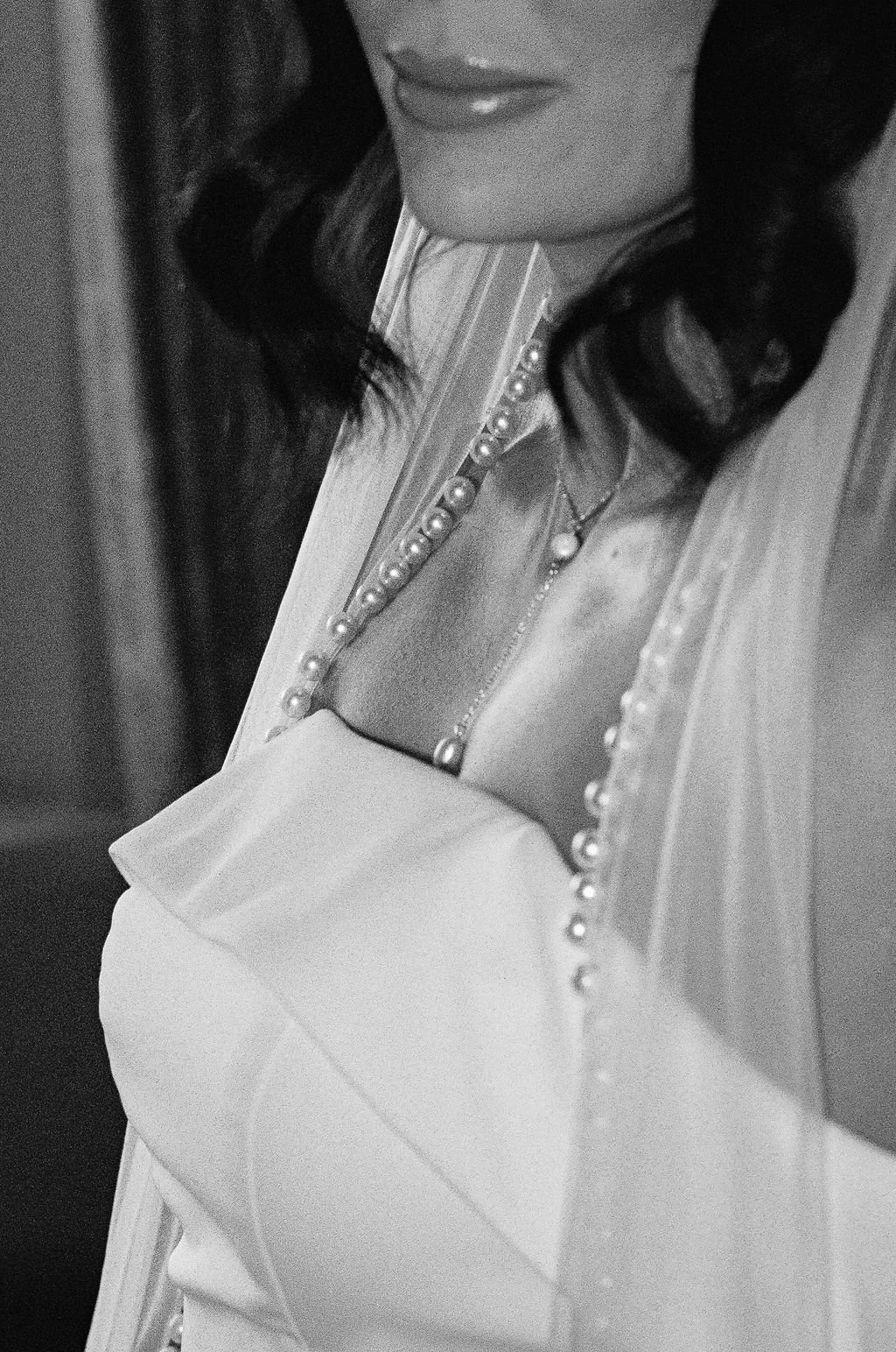 Close-up of a woman’s face and upper body, wearing a dress with a pearl and jeweled collar, in black and white.