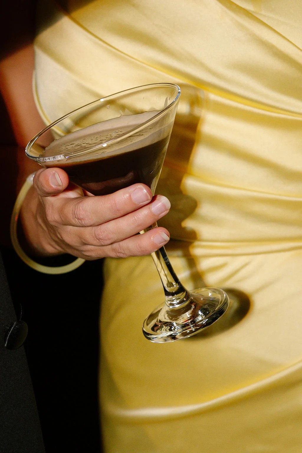 Person holding a glass of dark beer or stout in their hand, wearing a yellow outfit.