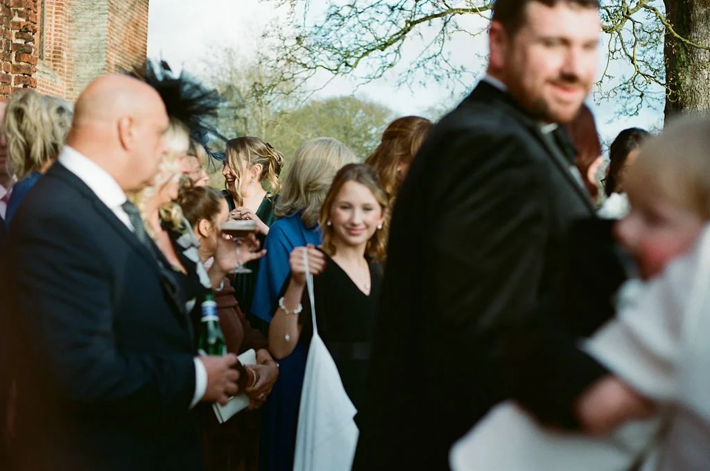 People gathered outdoors at a social event, possibly a wedding, with some holding drinks and smiling.