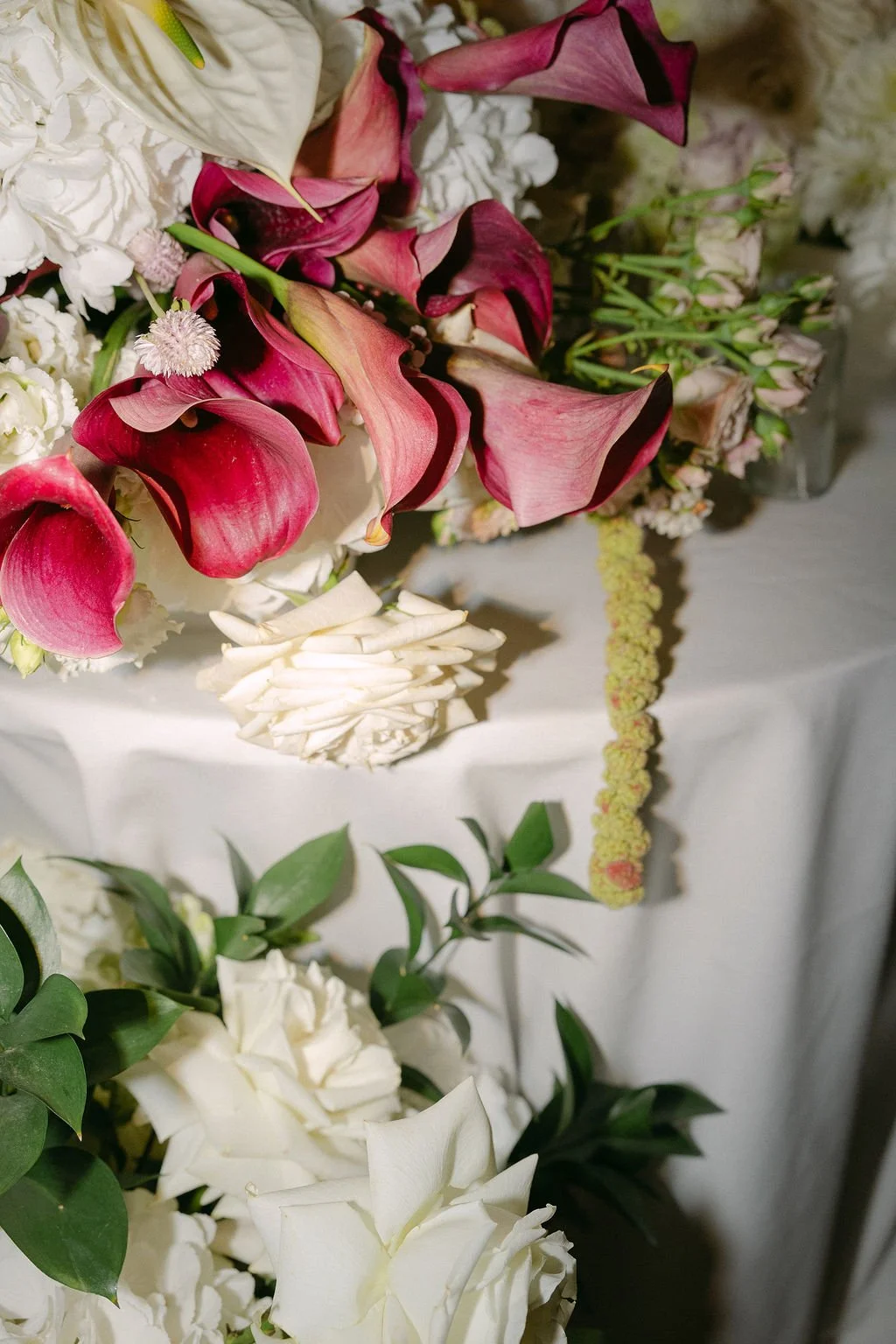 Close-up of various flowers, including pink calla lilies, white roses, and greenery, arranged together.