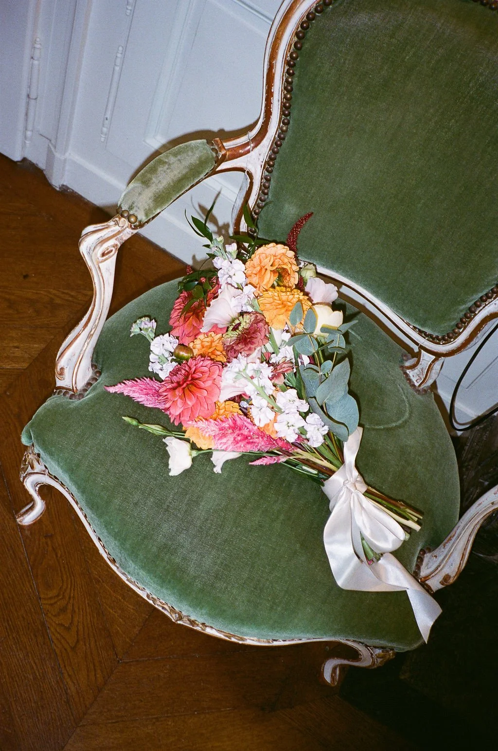 A bouquet of colorful flowers resting on an elegant antique green velvet chair with wooden frame and carved details.