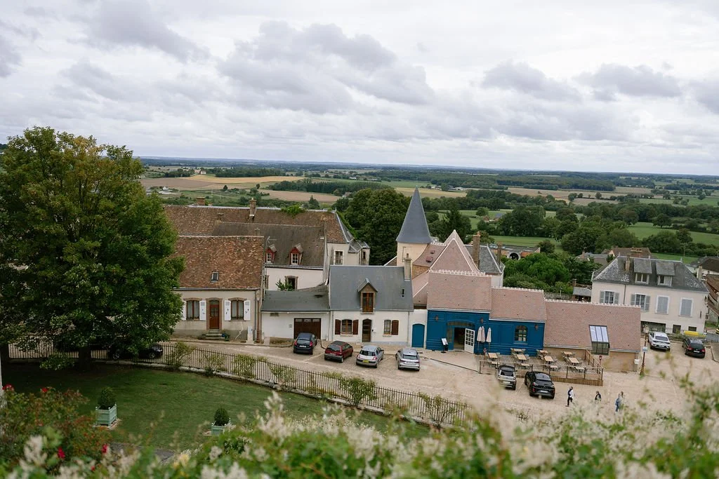 View of a small village with a church and houses, surrounded by green fields and cloudy sky.
