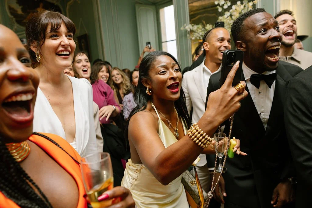 Group of people dressed in formal attire, laughing and enjoying themselves at an indoor celebration or party.