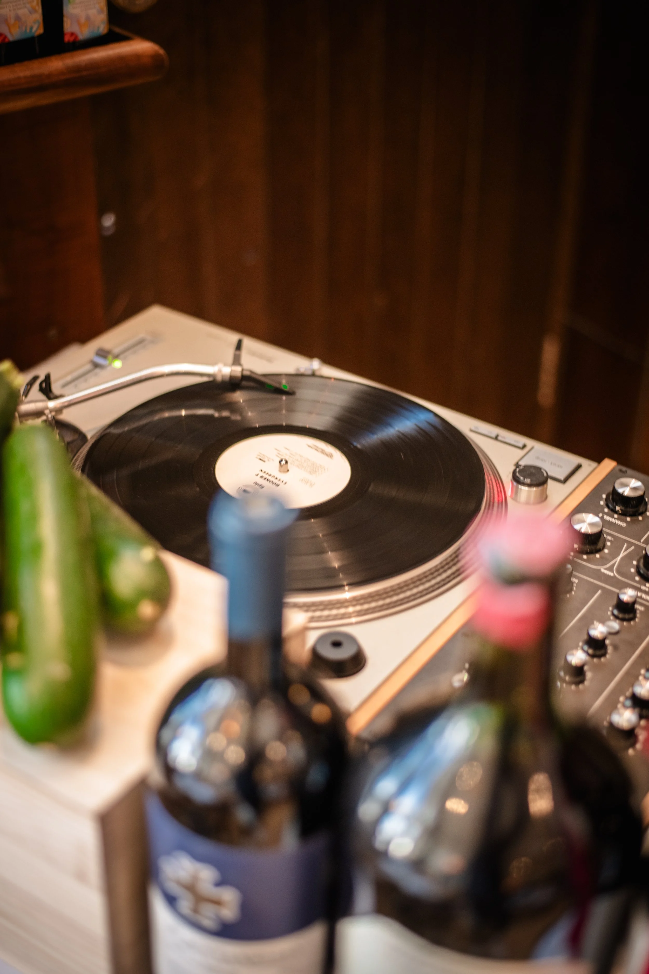 A DJ turntable with a vinyl record playing, surrounded by various bottles of beverages.