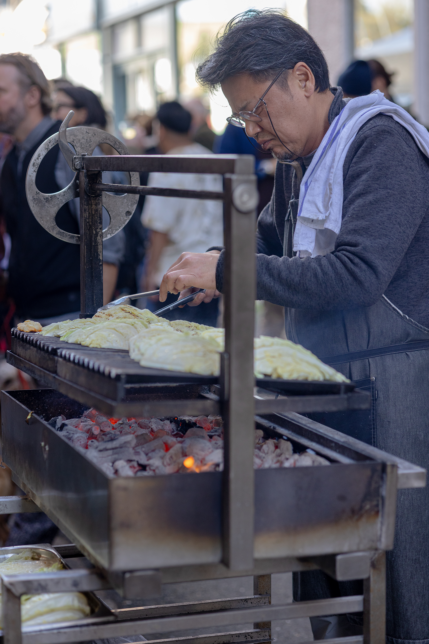 A man cooking eggs on a grill at an outdoor event, with a crowd of people in the background.