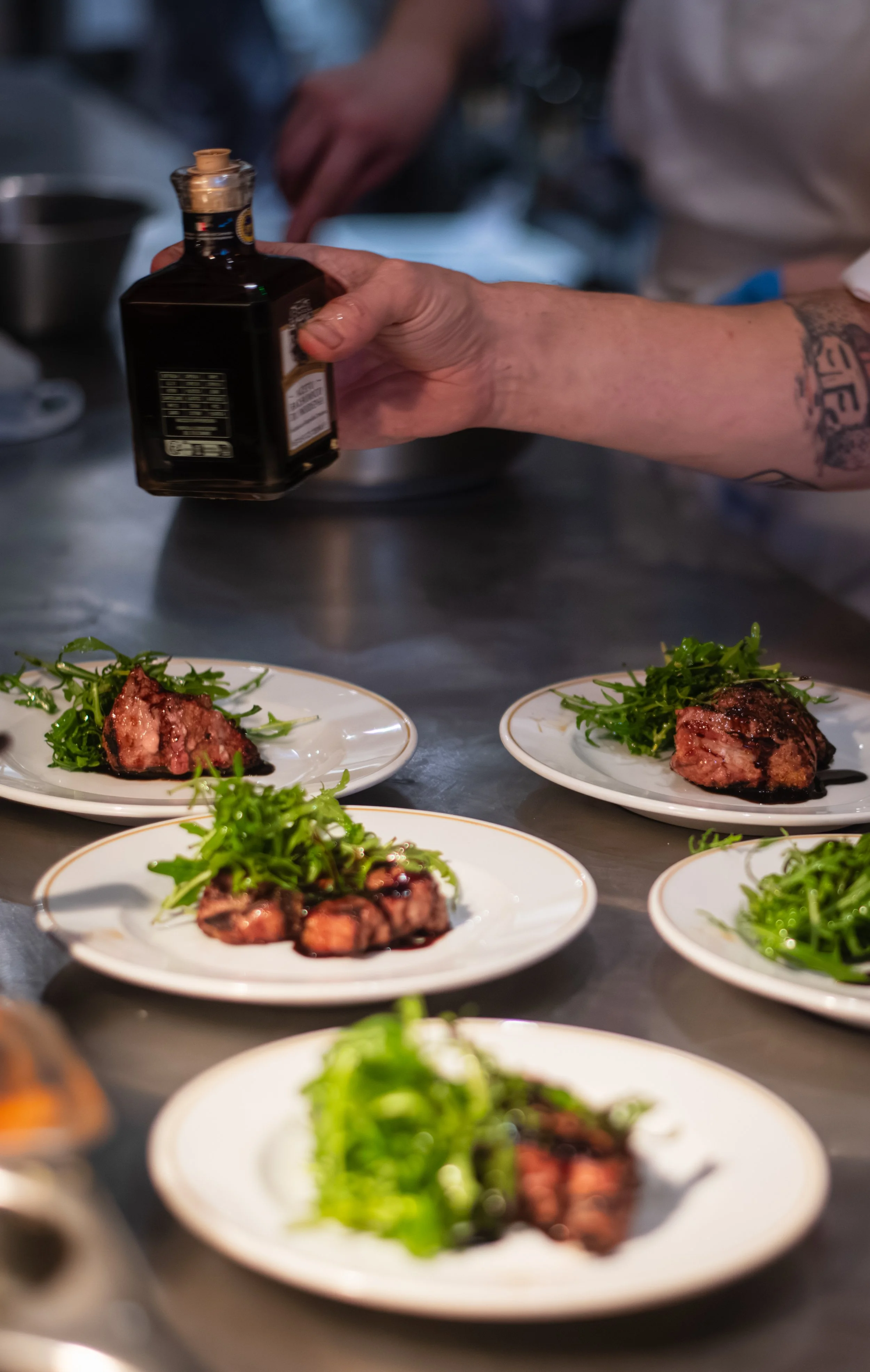 Chef garnishing plates of steak with arugula salad in a professional kitchen.