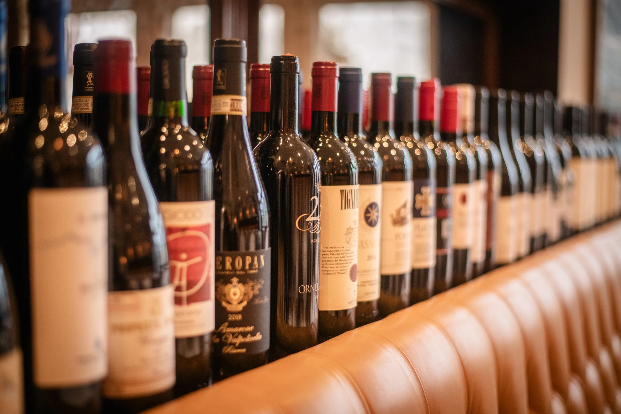 A row of wine bottles on a wooden shelf in a cozy setting.